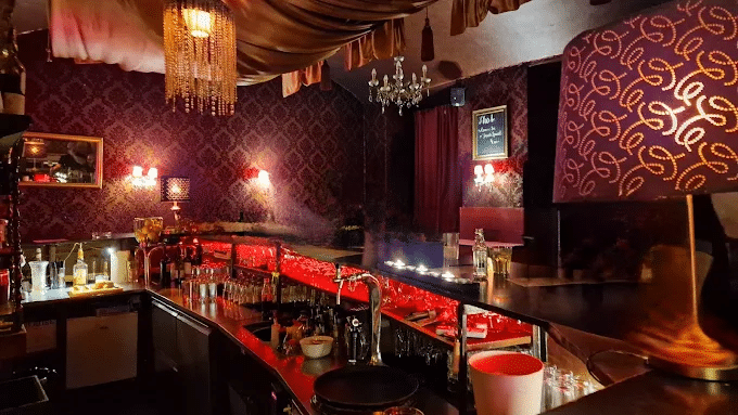 Red-lit bar at Tanzcafé Jenseits in Vienna with dark brocade wallpaper and crystal chandeliers